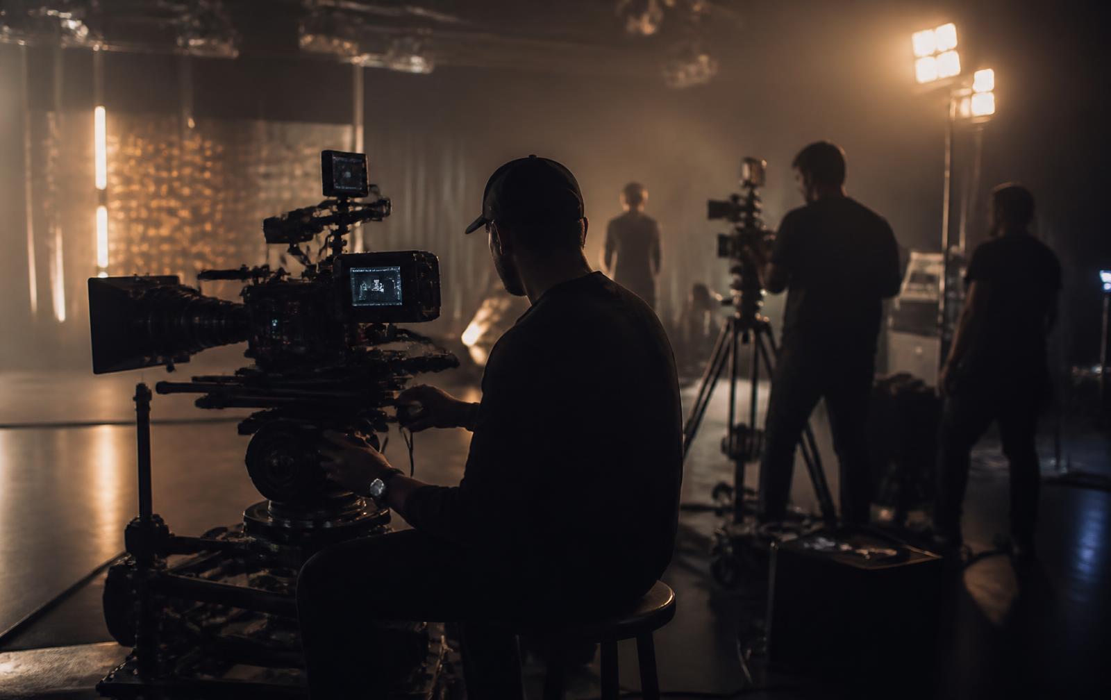 Cinematic film crew operating professional cameras and lighting on a dark soundstage